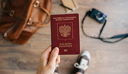 Person-holds-Russian-travel-passport-in-hand-with-leather-bag-and-photo-camera-in-the-back.jpg